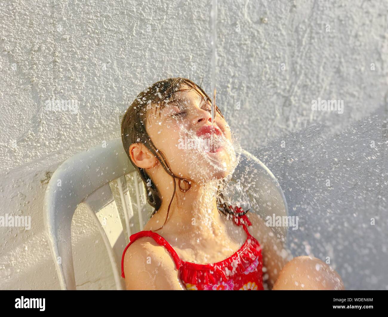 L'acqua spruzzata sulla bocca della ragazza contro il muro bianco Foto Stock
