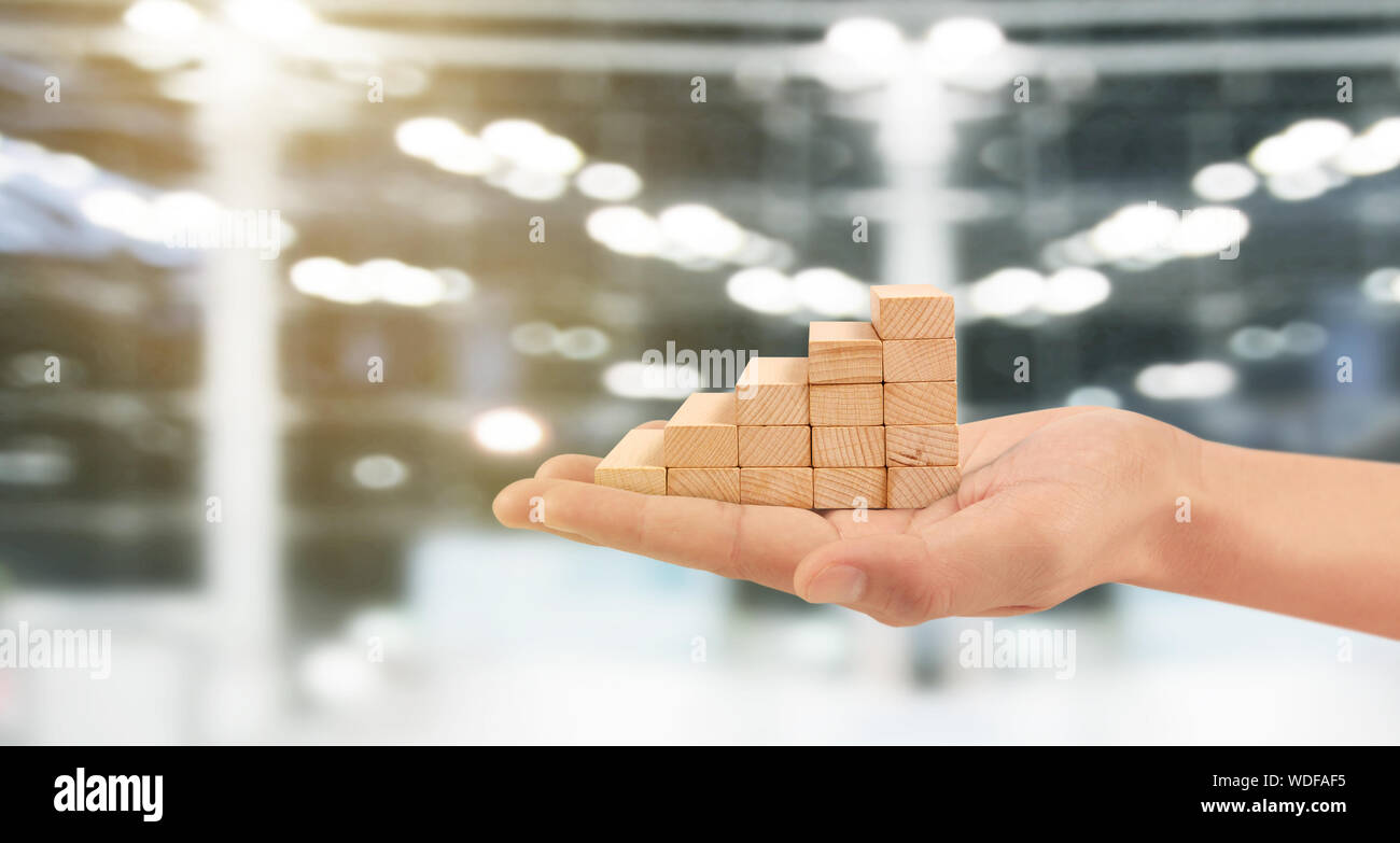 Blocco di legno come stacking passo gradino con freccia in su in una mano. Scaletta percorso di carriera concetto per la crescita del business processo di successo Foto Stock