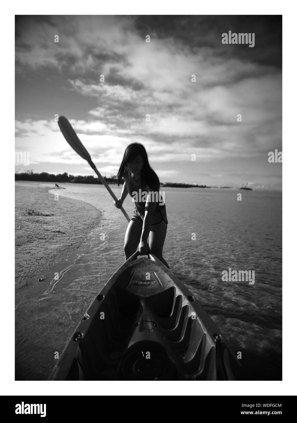 Donna tirando barca mentre la holding Oar on shore a Beach contro Sky Foto Stock
