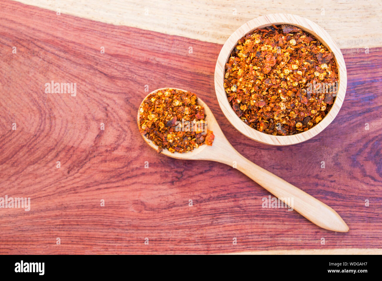 Speziato di pepe di cayenna in ciotola di legno e cucchiaio messo sul tavolo il legno duro. Selezionare la messa a fuoco. Foto Stock