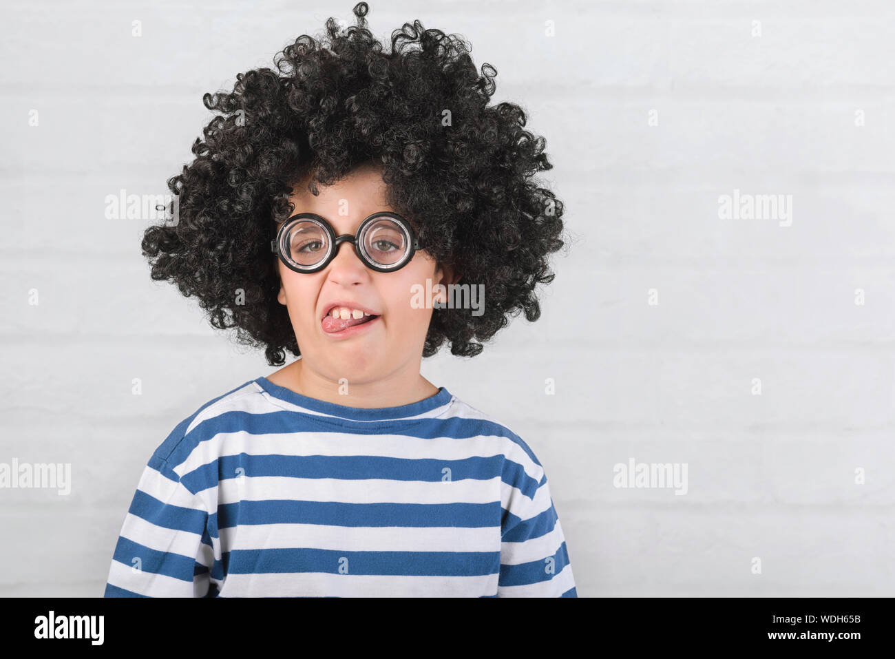 Funny bambino facendo una grimace indossando occhiali nerd su Sfondo mattone Foto Stock