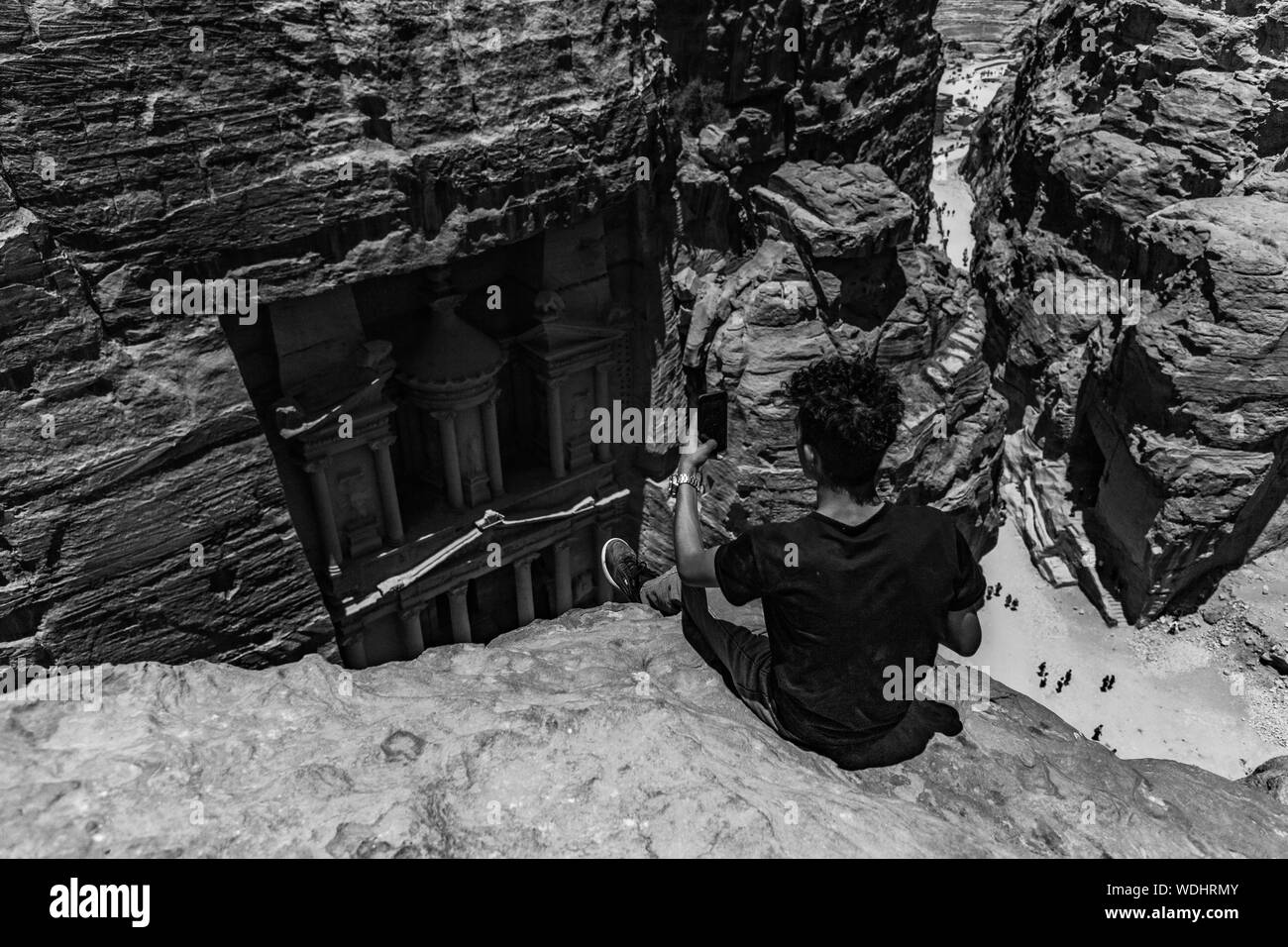 Una foto in bianco e nero di un giovane ragazzo di scattare una foto accanto al tesoro (Petra) come visto da un punto di vista vantaggioso. Foto Stock