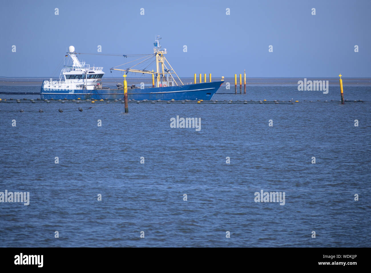 Barca da pesca presso l'artificiale cozza banche nel mare del Nord vicino a Friesland, Germania, copia spazio nell'acqua blu Foto Stock