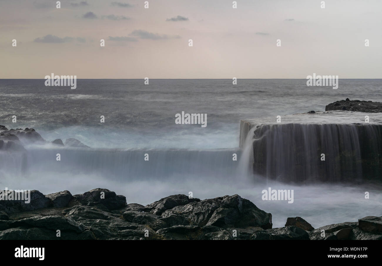 Mesa del Mar frangiflutti in cemento, fotografie con lunghi tempi di esposizione, onde passando sopra con il bianco setosa schiuma, Oceano Atlantico, i trend con orizzonte di riferimento e nuvole con tramonto Foto Stock