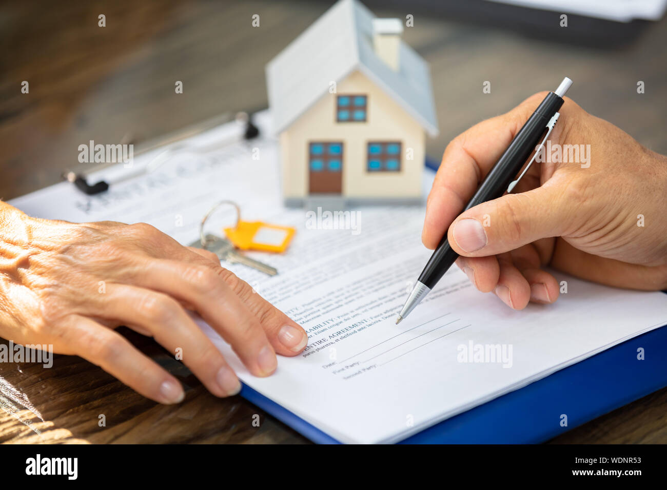Close-up di un agente immobiliare la mano aiutando Client nel riempire il modulo di appalto su scrivania Foto Stock