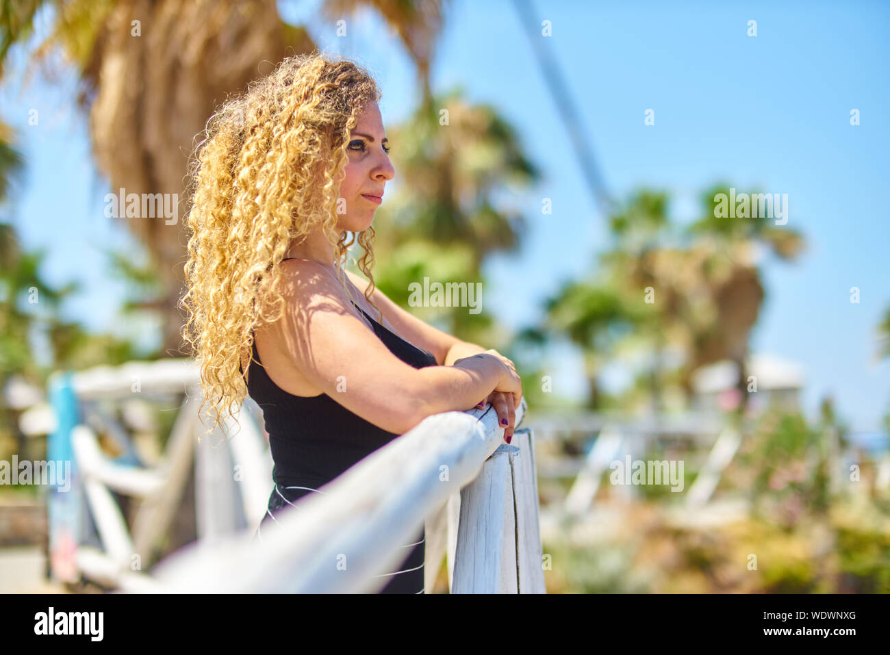 Considerato giovane donna bionda con capelli ricci in piedi dalla ringhiera contro Sky Foto Stock