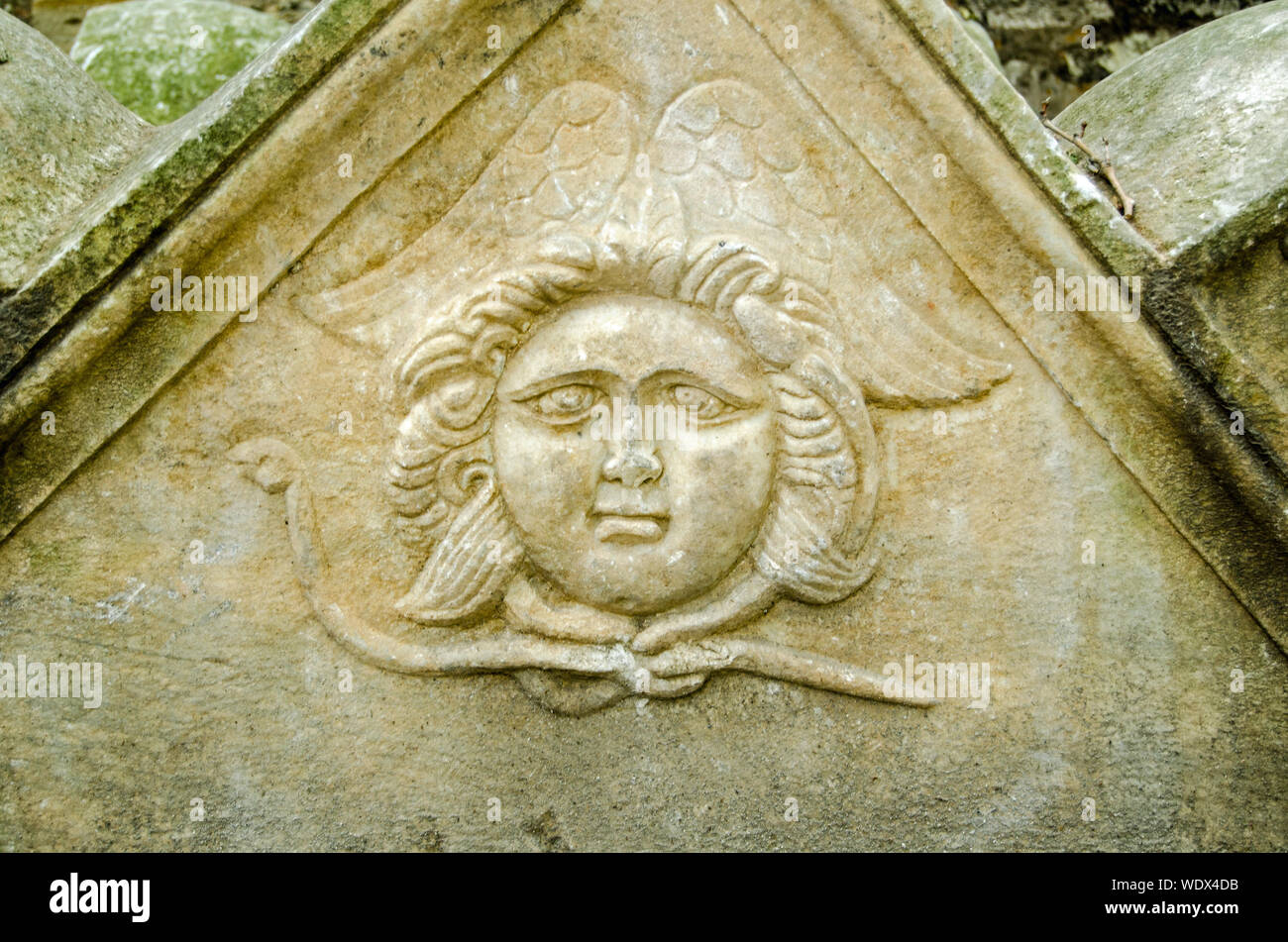 Un antica scultura di un angelo con un paffuto viso e ciò che appare come un serpente intorno al suo collo e le ali dietro. Sarcofago in pietra risalente al tardo Ro Foto Stock