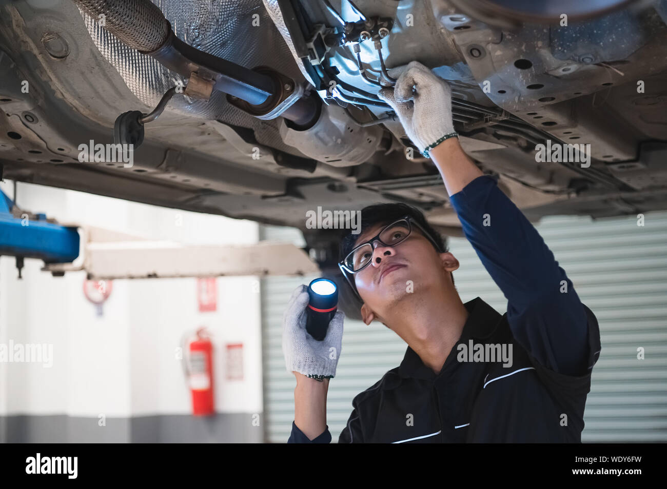 Maschio asiatici tenuta meccanica e luminosa torcia per esaminare auto sotto il telaio del veicolo automobilistico. Sospensione di sicurezza ispezione controllare service maint Foto Stock