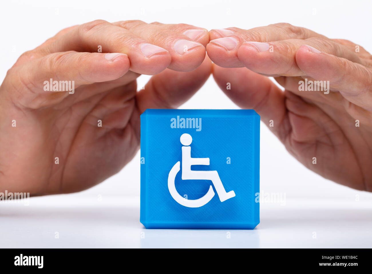 Close-up di una mano di un uomo la protezione blu blocco cubico con disabili Icona Handicap Foto Stock