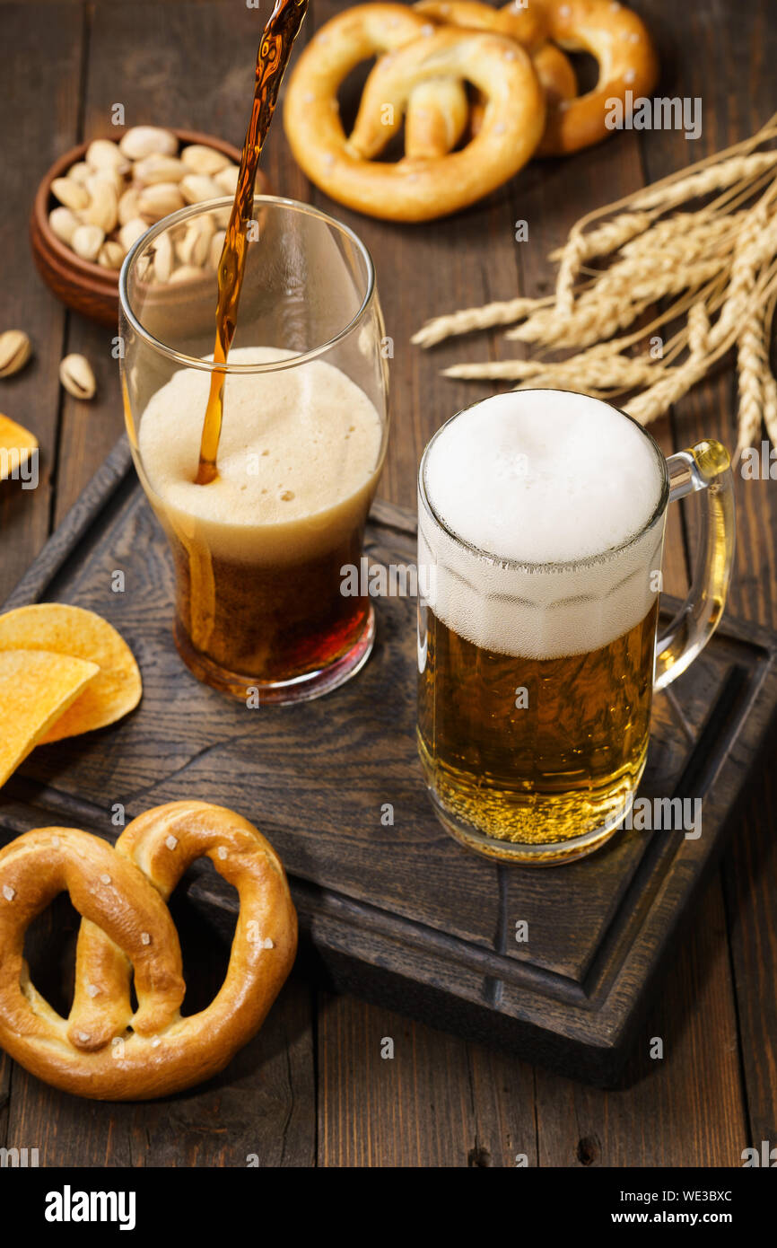 Vari tipi di birra appena spillata - luce e buio e varietà di snack. Legno scuro dello sfondo. Foto Stock