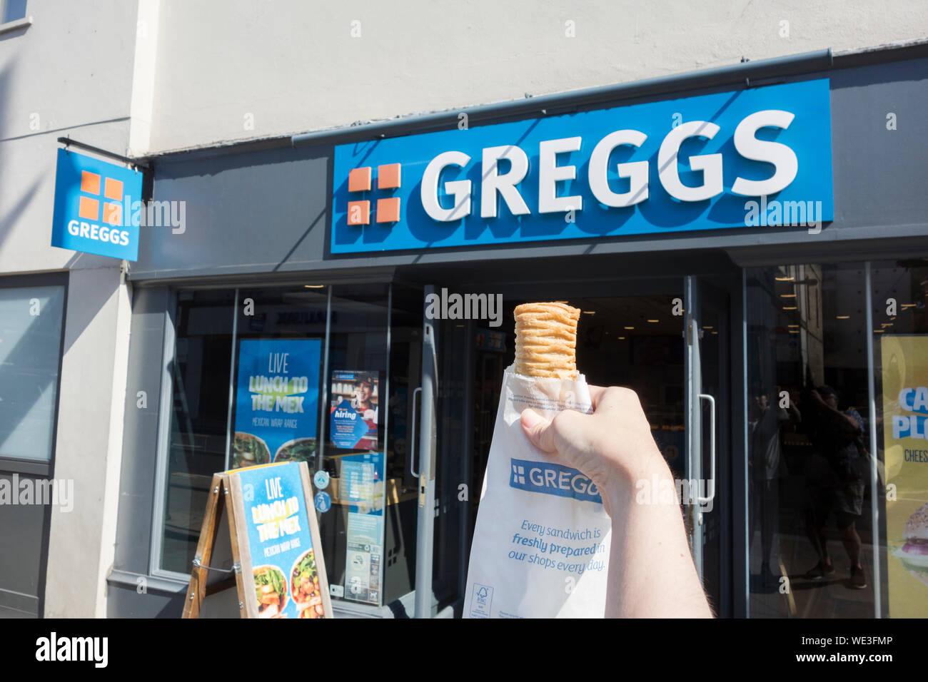 Una giovane donna di mano che tiene un vegano Greggs-friendly rotolo di salsiccia al di fuori di un Greggs a Richmond, Surrey, Regno Unito Foto Stock