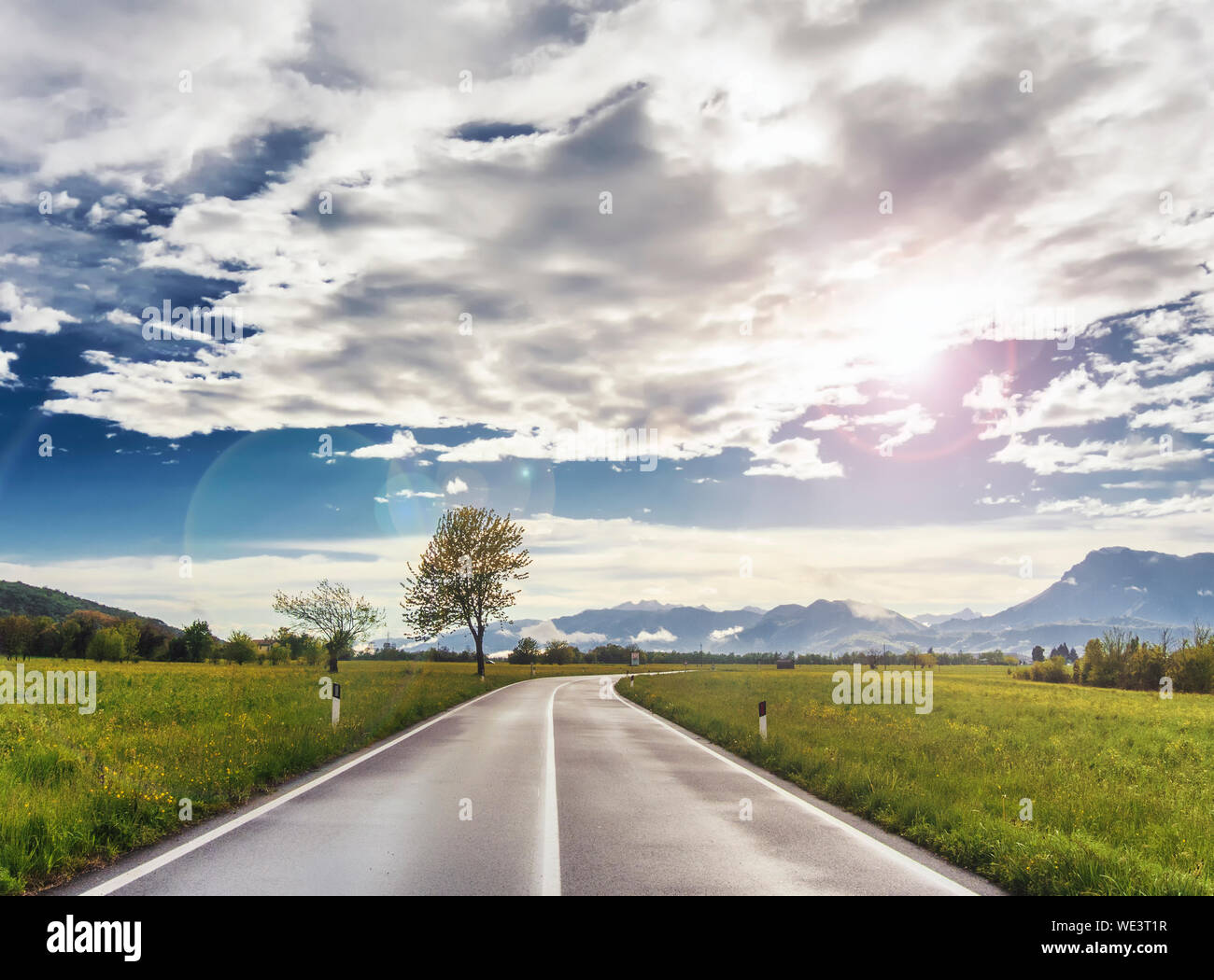 Strada vuota all orizzonte con verdi campi intorno, cielo blu e monti all'orizzonte. Bellissimo paesaggio dopo la pioggia a Pordenone, Italia Foto Stock