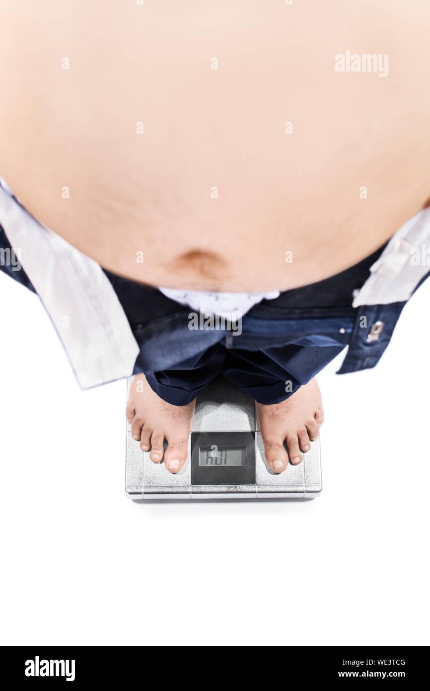 Vista dall'alto di un giovane maschio con grande stomaco e problemi di peso in piedi su una scala, isolato su sfondo bianco. Foto Stock