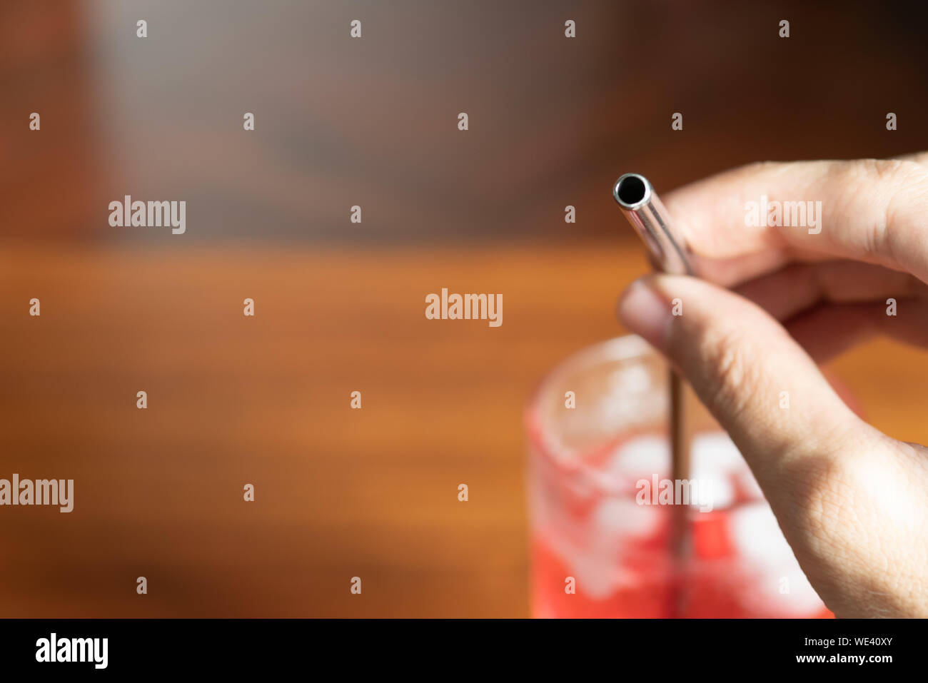 Mano che tiene la paglia di metallo in un bicchiere di rosso bevanda dolce Foto Stock