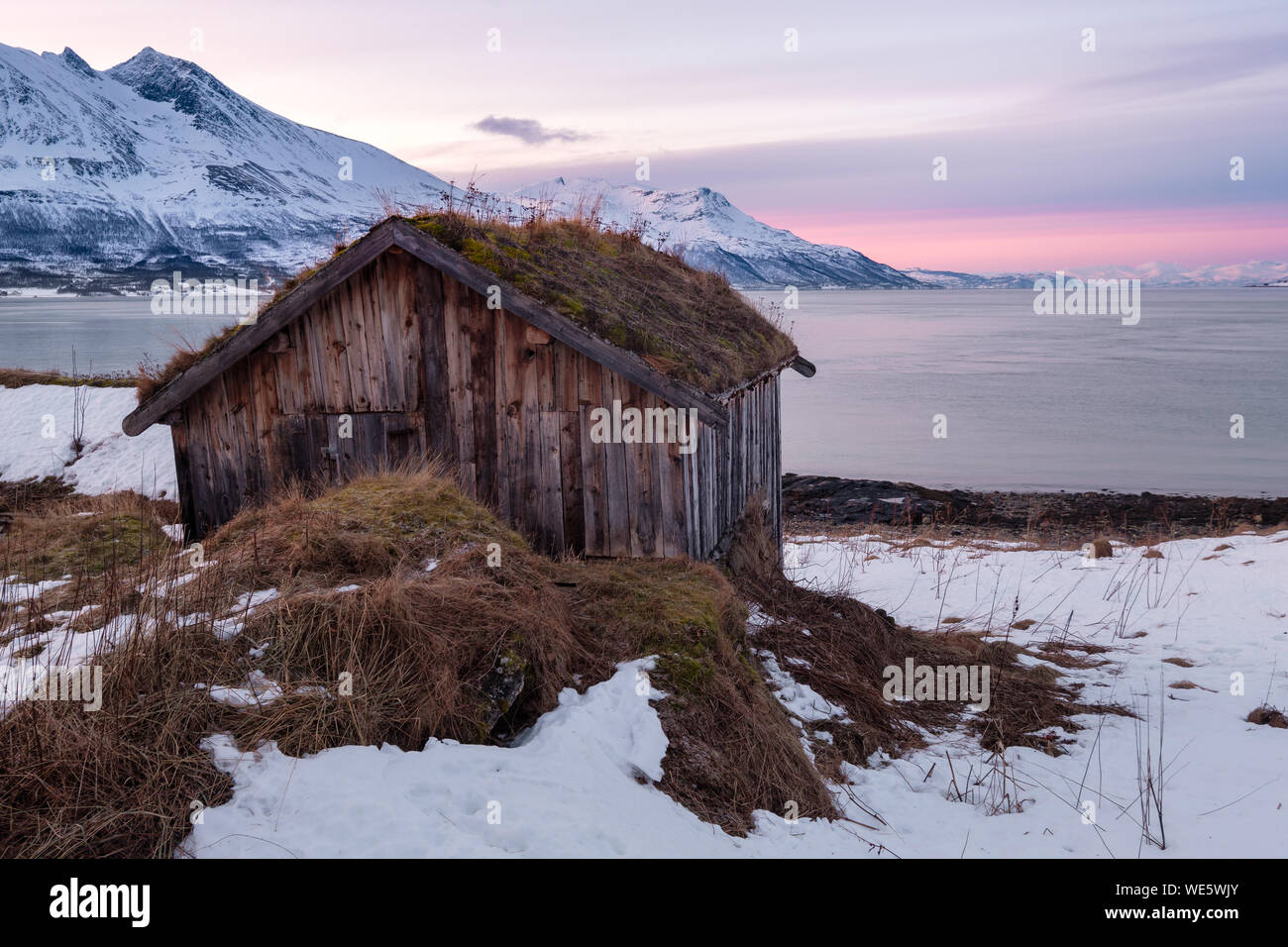 Artic paesaggio in un fiordo con la vecchia capanna sotto il cielo rosa al tramonto, Tromsö, Norvegia Foto Stock
