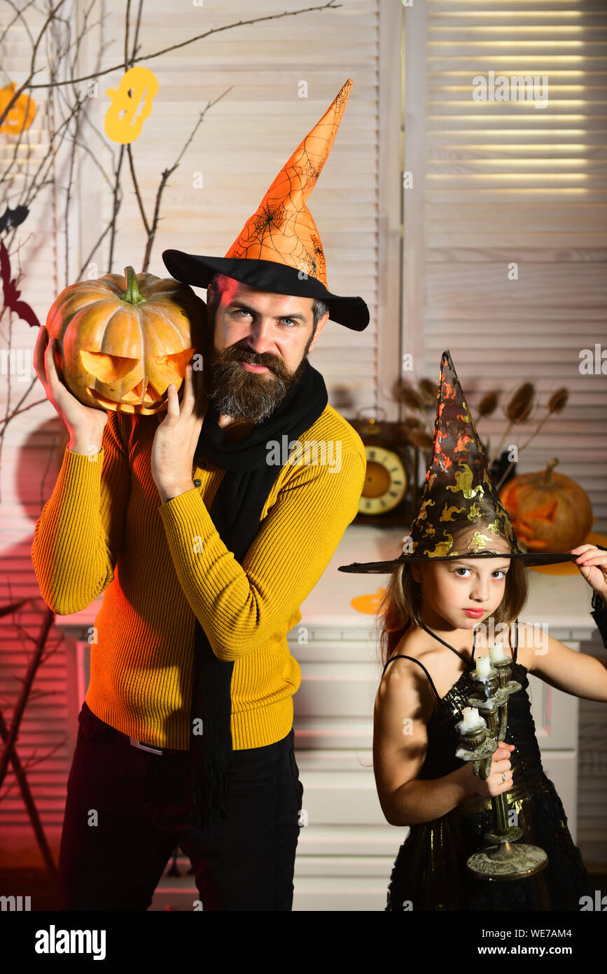 Papà e capretto in cappelli di strega tenere la zucca e lampadario. Festa  di Halloween concetto. Ragazza e uomo barbuto con volti sorridenti su red  spooky camera carnevale ba Foto stock -