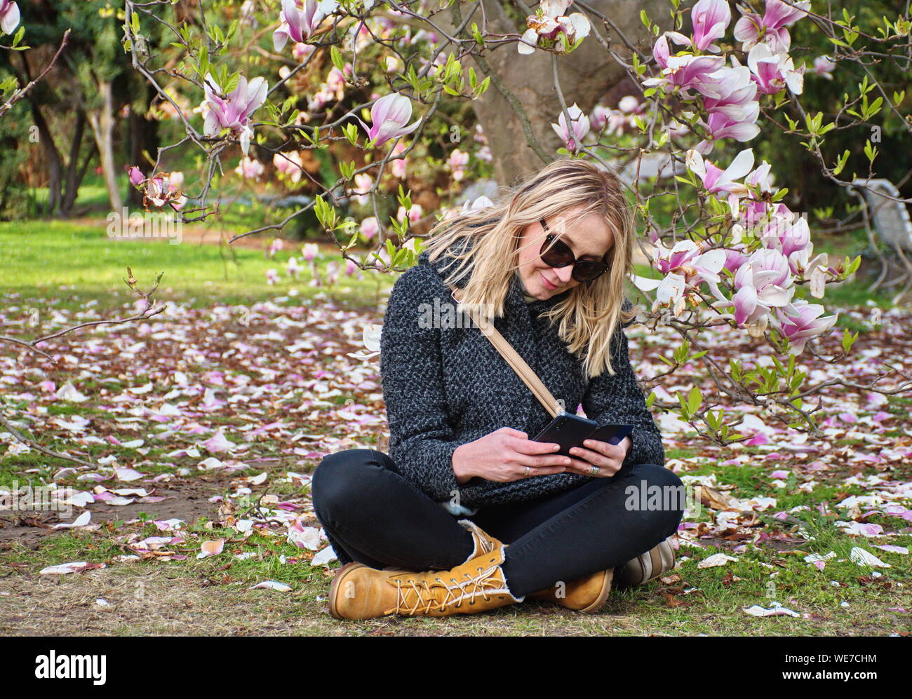 Ritratto di giovane donna seduta nel parco sotto albero di magnolia Foto Stock