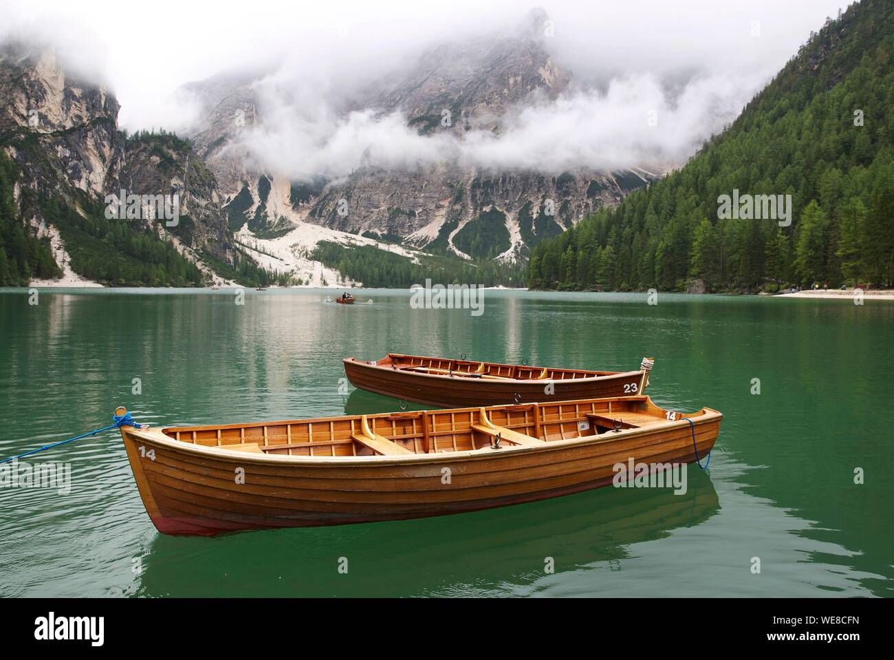 L'Italia, provincia autonoma di Bolzano, Alta Pusteria, il lago di Braies, barche sulle acque color smeraldo del lago circondato da montagne verdi catturati nella nebbia Foto Stock