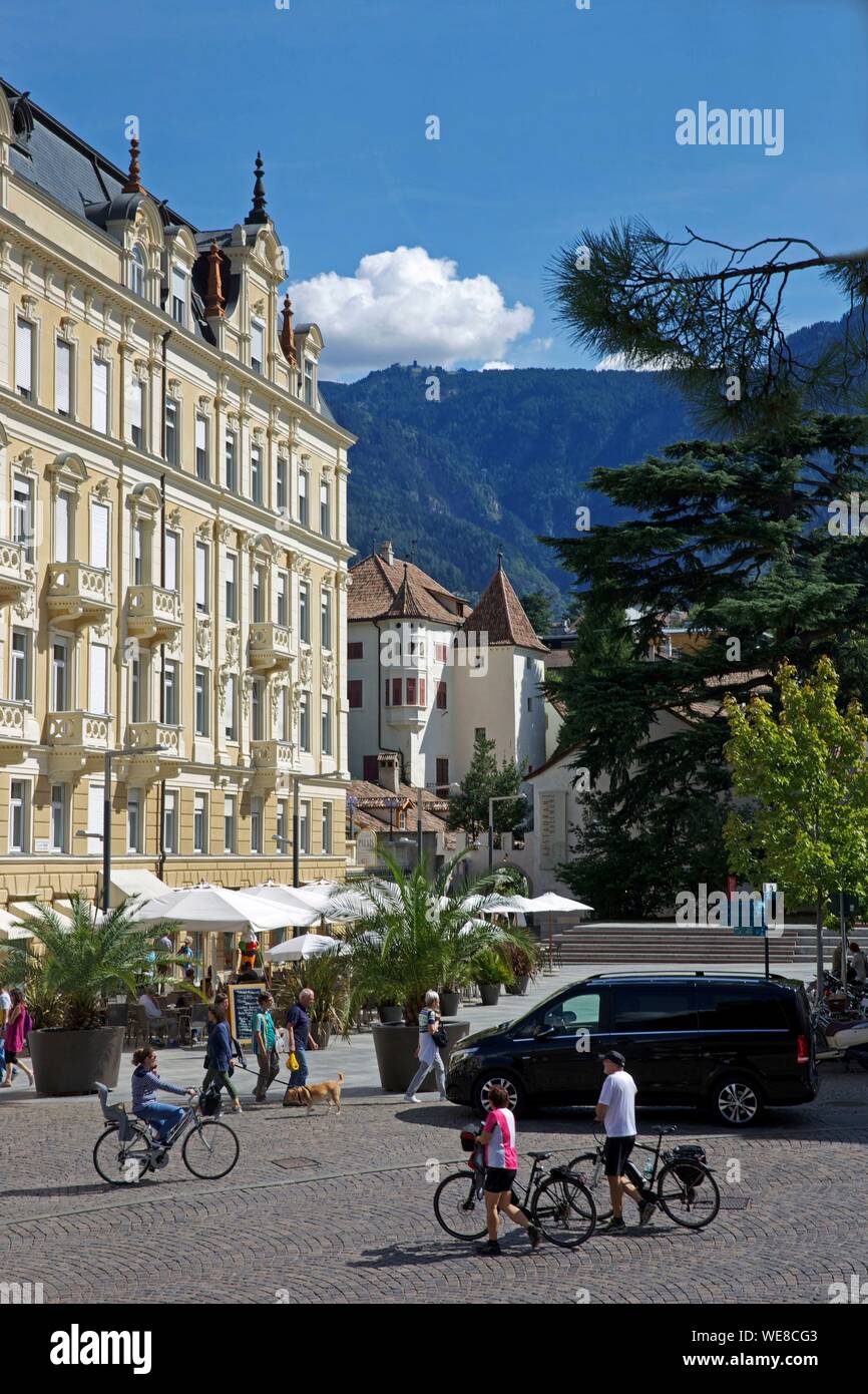 L'Italia, provincia autonoma di Bolzano, Merano, ciclisti di fronte ad un edificio neoclassico downtown con montagne verdi in background Foto Stock