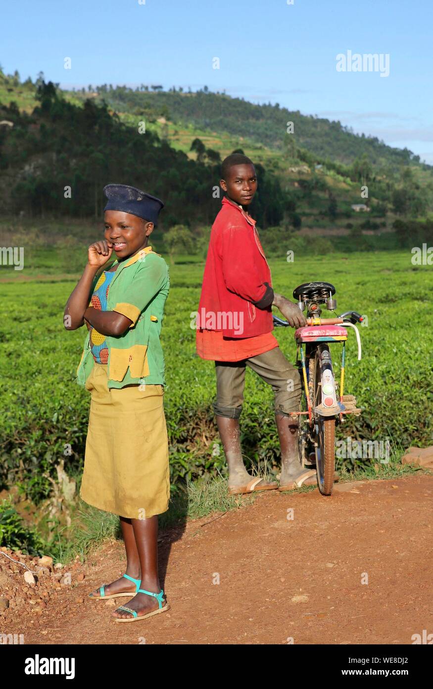 Il Ruanda, al centro del paese, bambini in abiti colorati su una pista di laterite in mezzo al verde delle colline Foto Stock