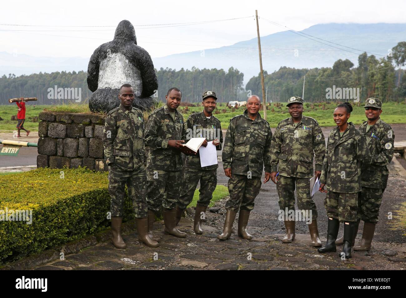 Ruanda, Parco Nazionale Vulcani, lattice rangers all'entrata del Parco Nazionale Vulcani in posa di fronte a una gigantesca statua di gorilla di montagna Foto Stock