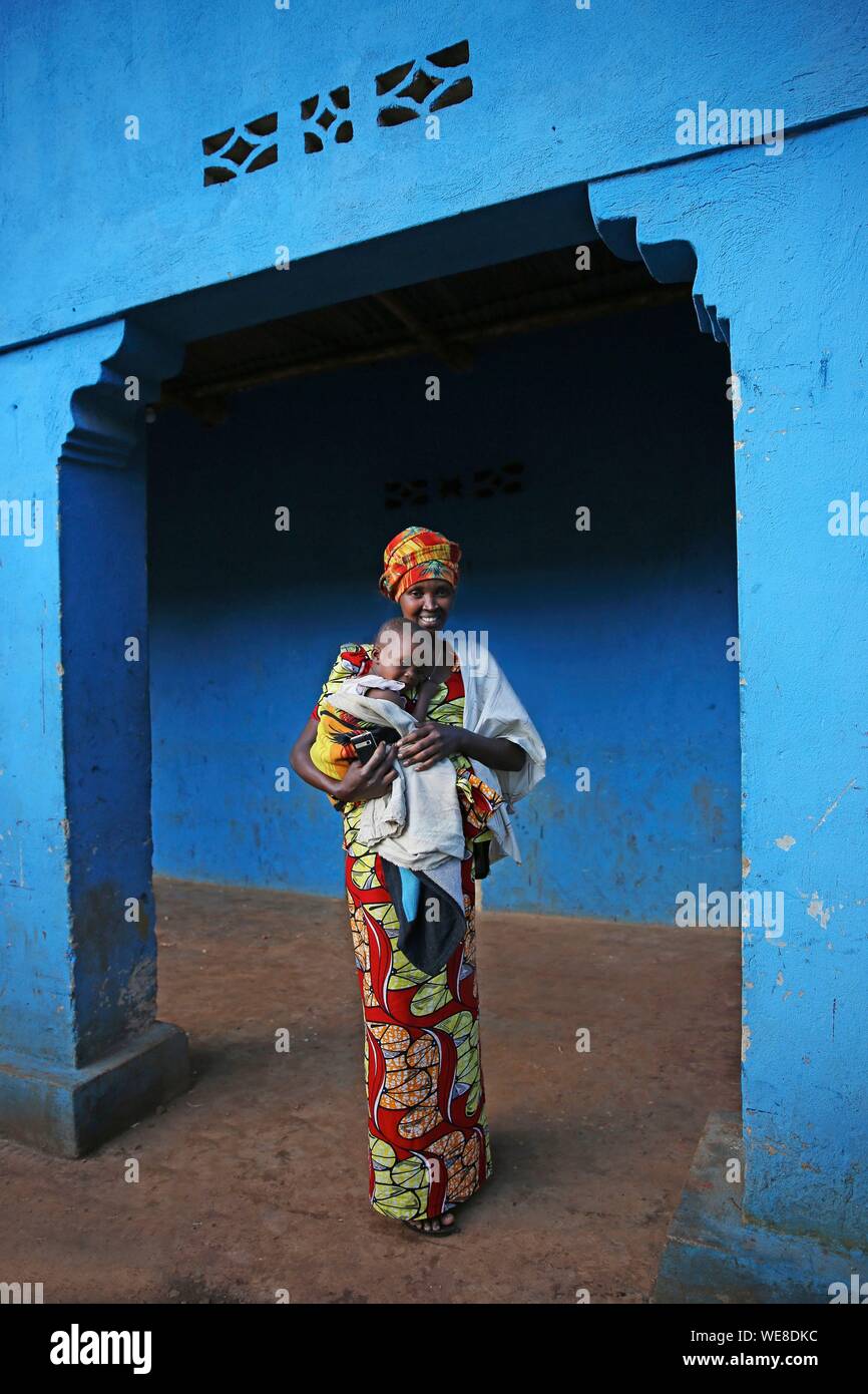 Il Ruanda, al centro del paese, donna in colorate perizoma con il suo bambino nelle braccia di fronte al muro di una casa blu Foto Stock