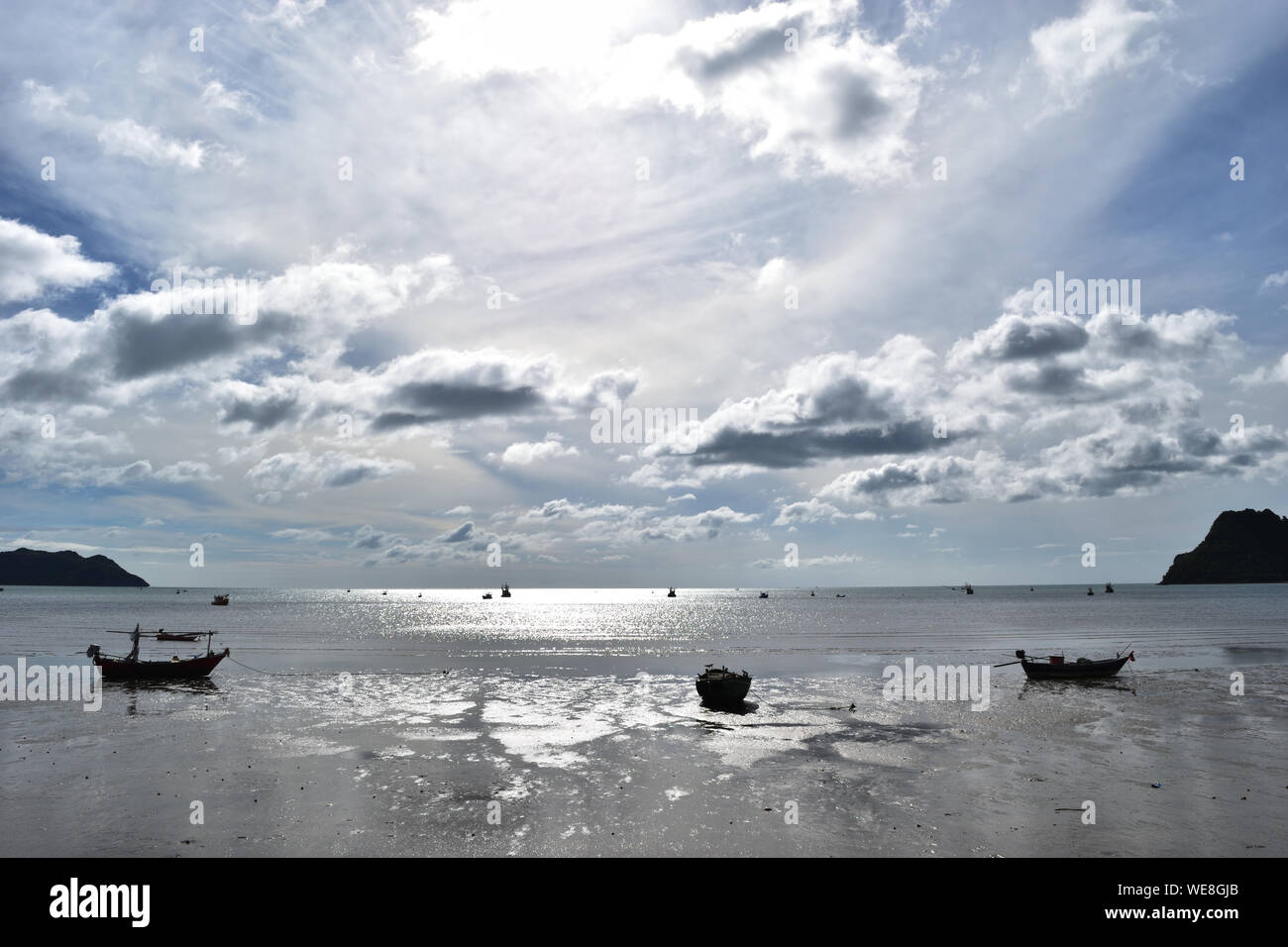 Barche da pesca in mare e sulla costa, Prachuap Bay sul mare liscio giorno e il cielo pieno di nuvole, superficie di acqua è pieno di luce scintillante Foto Stock