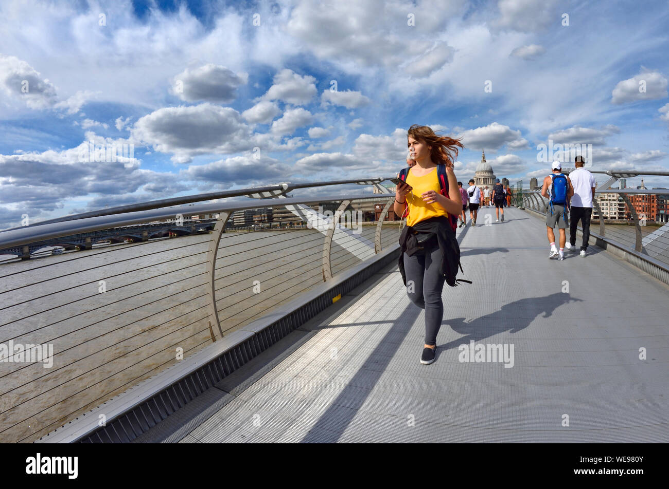 Londra, Inghilterra, Regno Unito. Giovane donna attraversando il Millennium Bridge in una giornata di sole nel mese di agosto Foto Stock