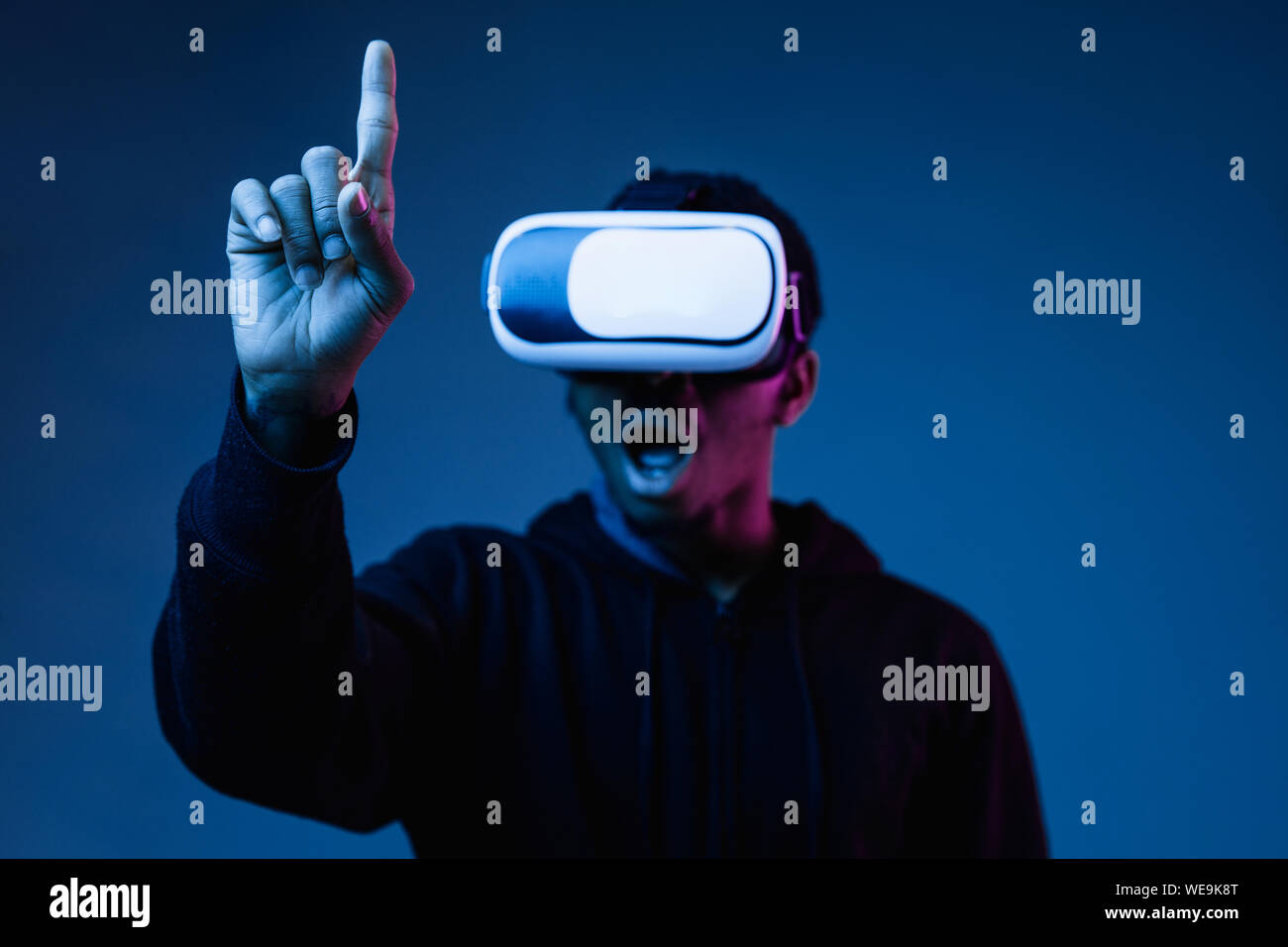 Giovani afro-americano in VR-bicchieri in una luce al neon su sfondo blu. Ritratto maschile. Concetto di emozioni umane, espressione facciale, gadget moderni e tecnologie. Toccare vuota la barra di ricerca. Foto Stock