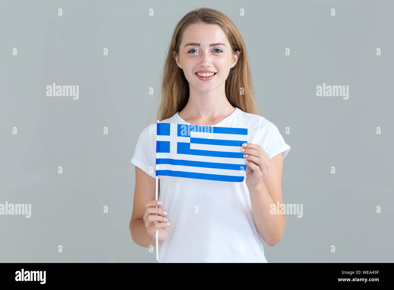 Giovane donna con bandiera della Grecia in mano isolato su sfondo grigio. Viaggi e Istruzione. Foto Stock
