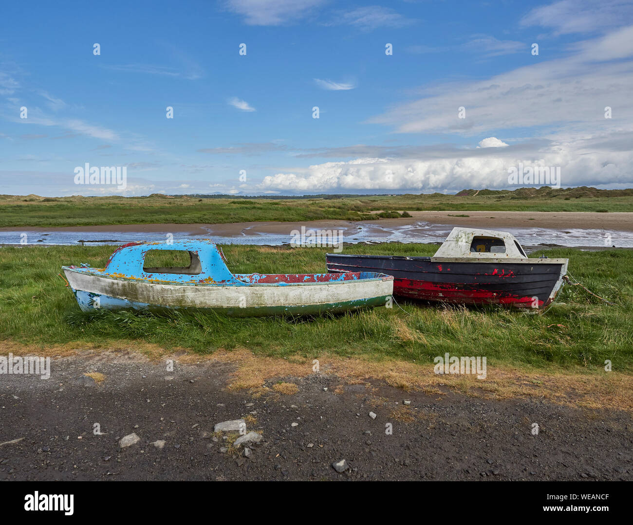 Due vecchie piccole barche da pesca insieme sat su erba accanto a un fiume con la marea sull'Isola di Anglesey, Galles del Nord, Regno Unito Foto Stock