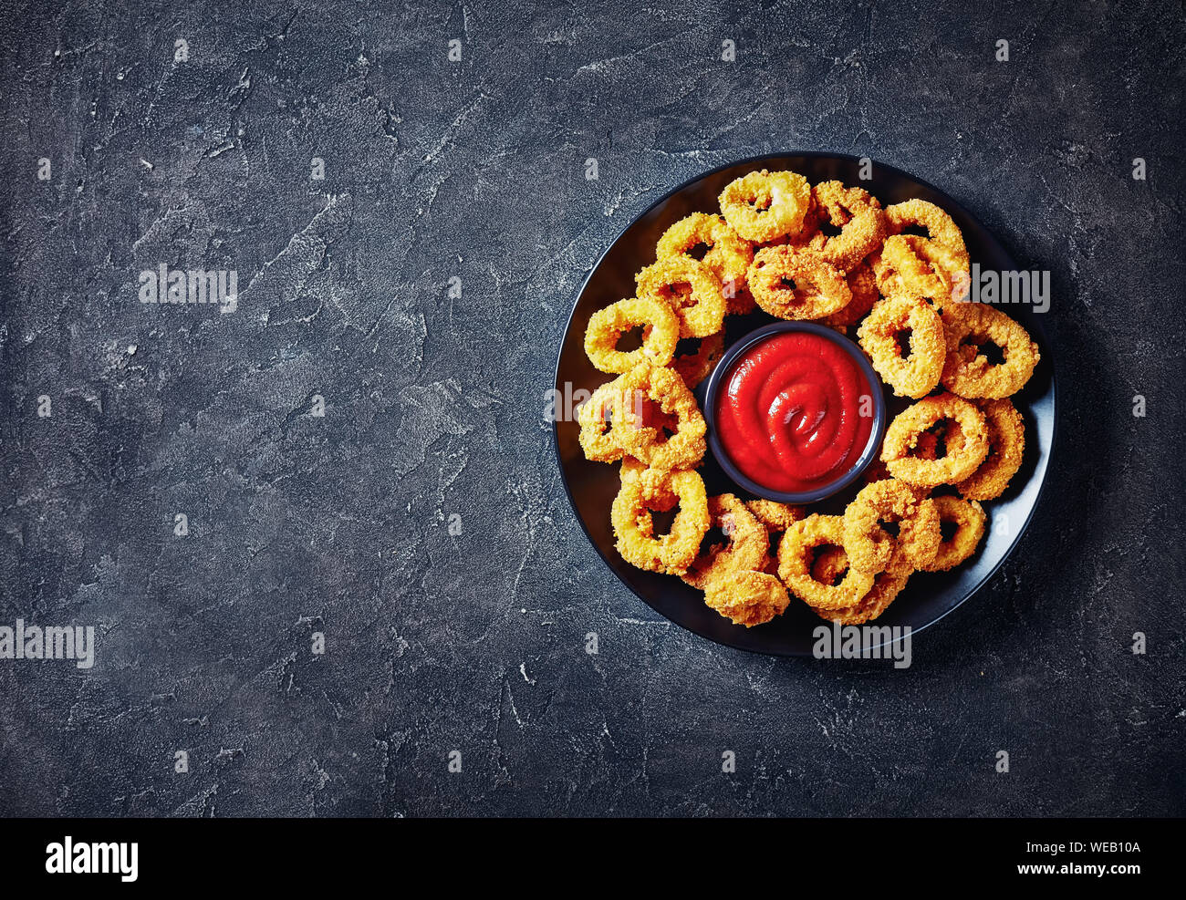 Croccanti anelli di calamari, fritte panate anelli di totano servito con salsa di pomodoro su una piastra nera su una tavola di cemento, vista orizzontale dal di sopra, libero Foto Stock