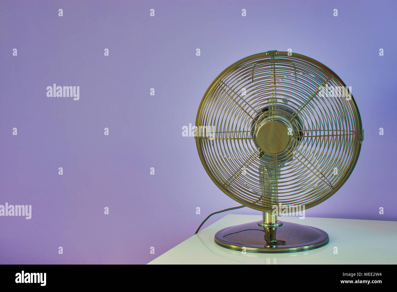 Ventilatore su un tavolo bianco di fronte a un muro viola con spazio di copia Foto Stock