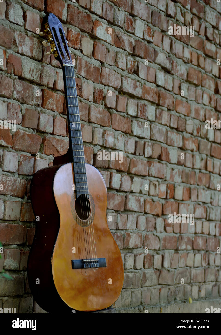La chitarra classica appoggiata contro un vecchio muro di mattoni Foto Stock