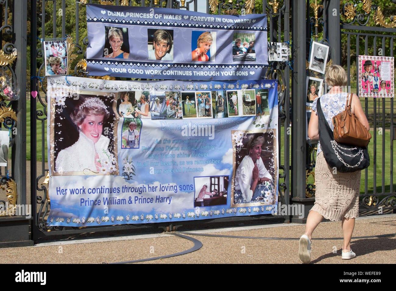 Una donna cammina oltre i cancelli di Kensington Palace a Londra, dove le persone hanno attaccato i poster e le foto della principessa Diana, come l anniversario della sua morte è previsto essere segnato dalla famiglia, amici e fans sabato. Foto Stock