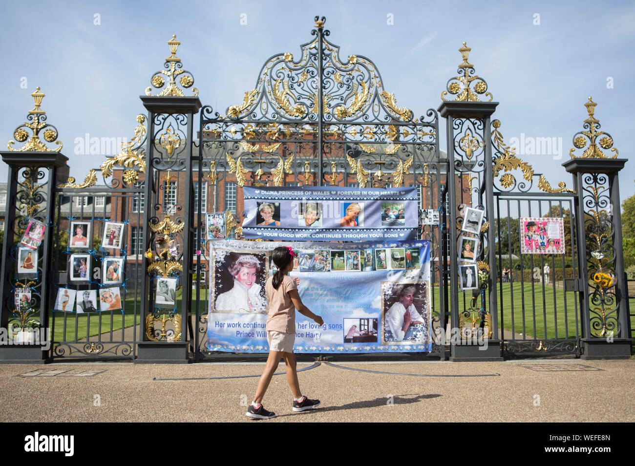 Una giovane ragazza cammina oltre i cancelli di Kensington Palace a Londra, dove le persone hanno attaccato i poster e le foto della principessa Diana, come l anniversario della sua morte è previsto essere segnato dalla famiglia, amici e fans sabato. Foto Stock