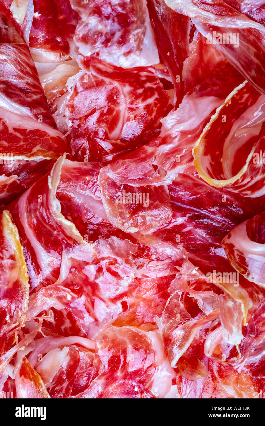 Stuzzicanti fette di prosciutto iberico in primo piano come una texture. La carne cruda che diventa un articolo di alta cucina gastronomica e di lusso, attraverso una proc Foto Stock