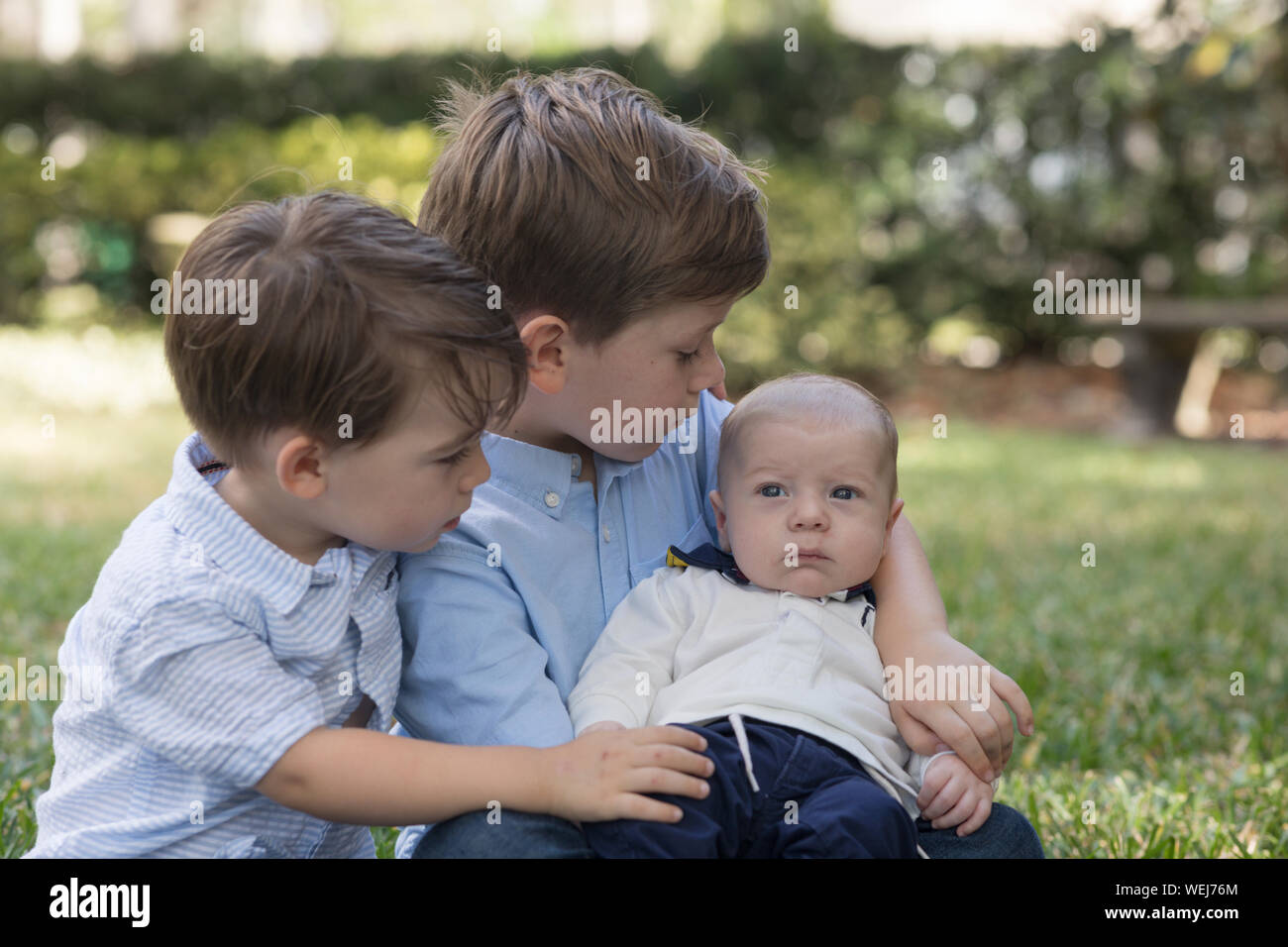 Due ragazzi, 4 anni e 2 anno di età, tenendo il loro bambino fratello in un parco Foto Stock