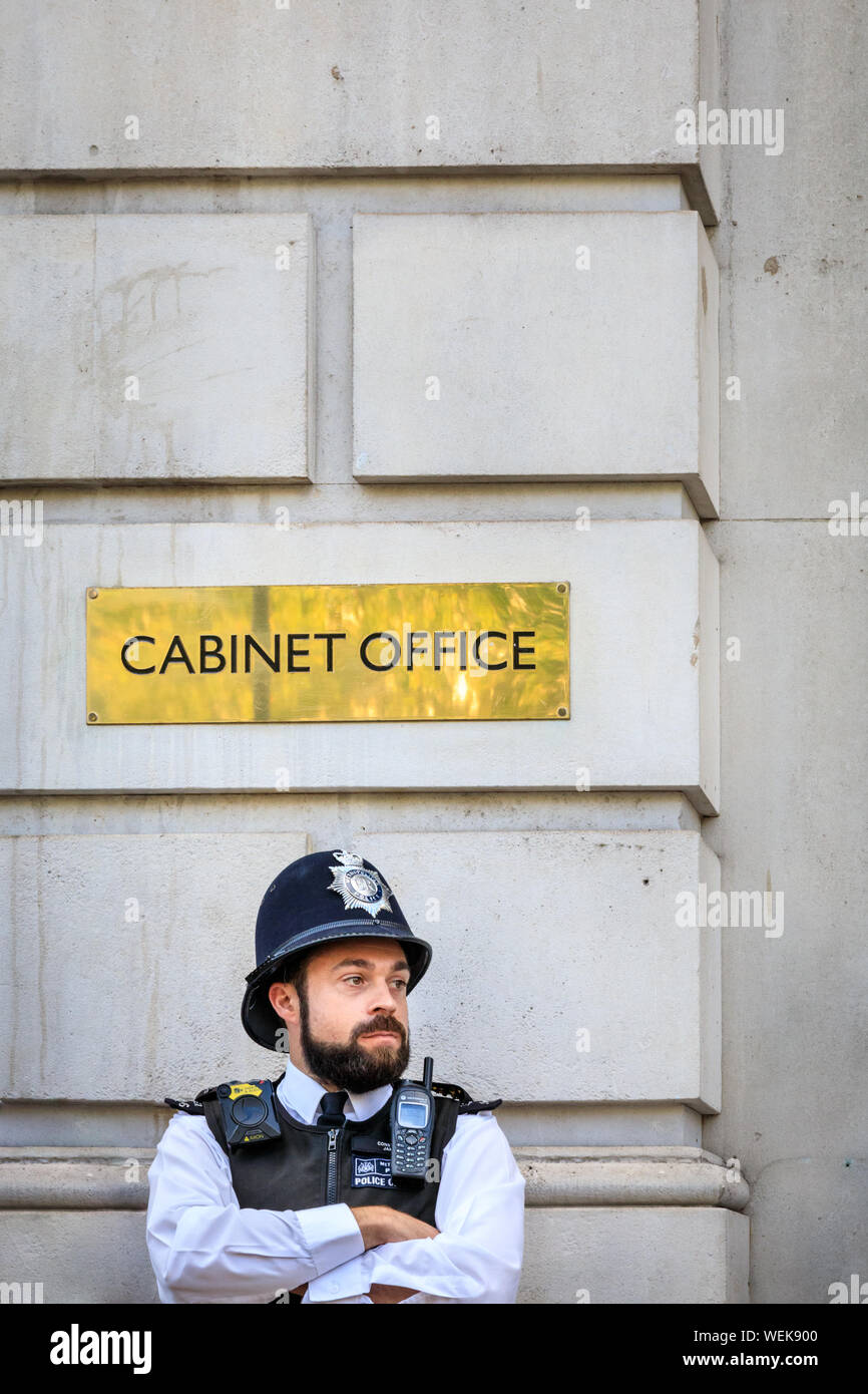 La Metropolitan Police officer, poliziotto in piedi al di fuori del Cabinet Office segno su Whitehall, Westminster, London, Regno Unito Foto Stock