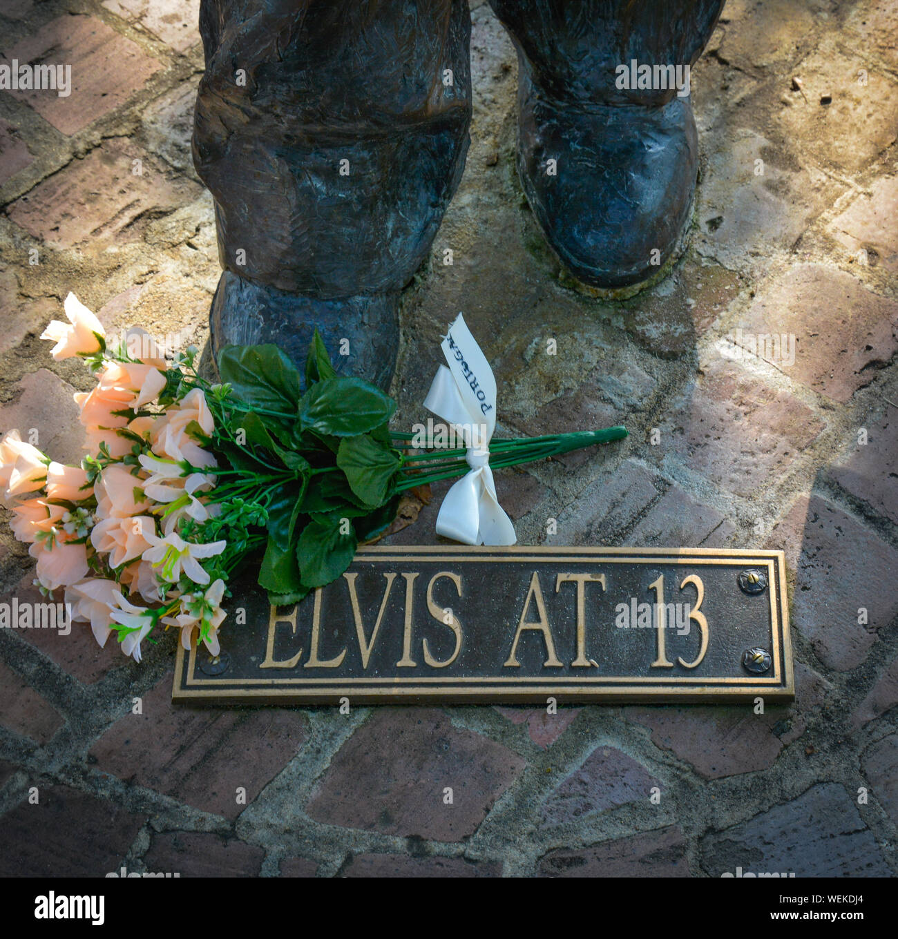 Close up dei piedi di una statua di bronzo di Elvis Presley in 13 con signage ai suoi piedi con fiori nella sua città natale museum di Tupelo, MS Foto Stock