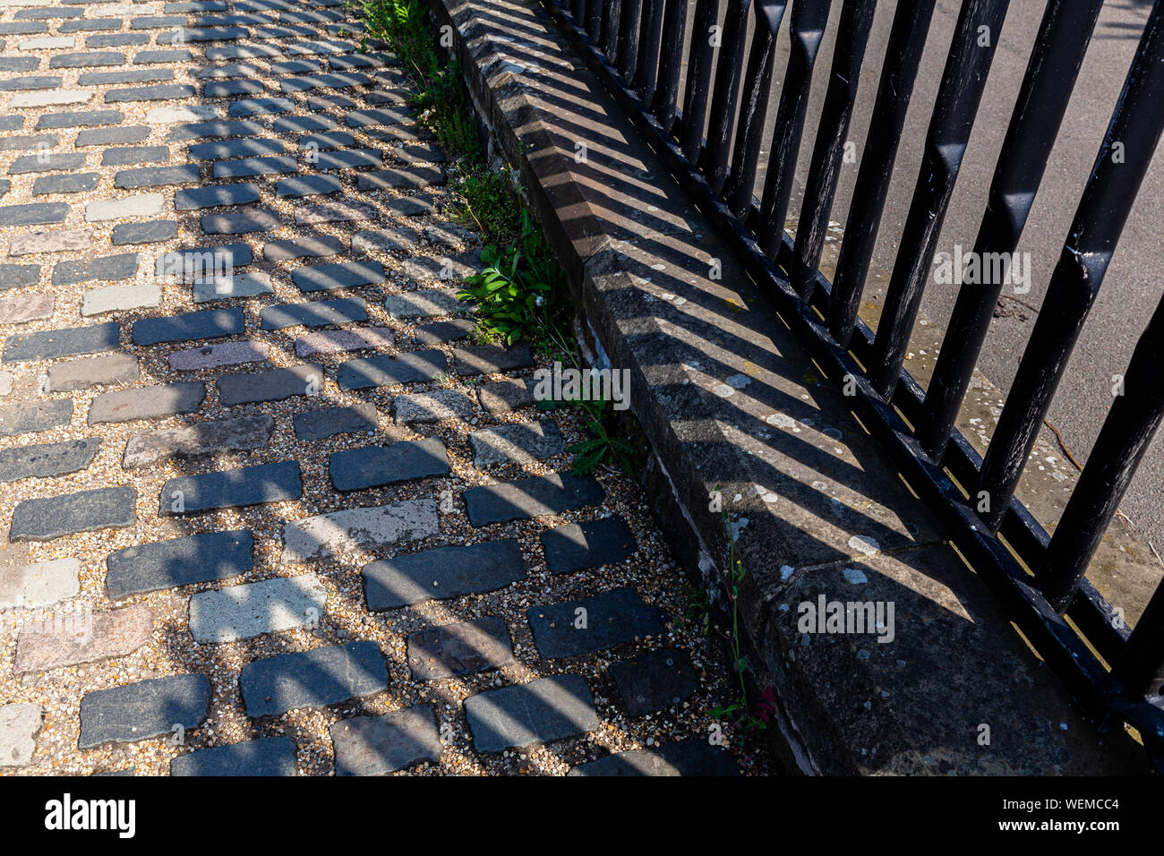 Pali recinzione con lunghe ombre su un percorso di pietra Foto Stock