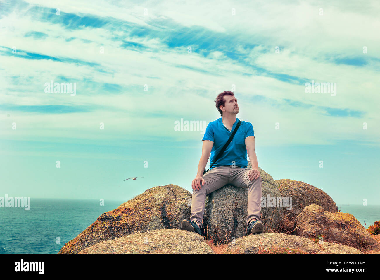 Uomo seduto su di una roccia al mare guardando in alto Foto Stock