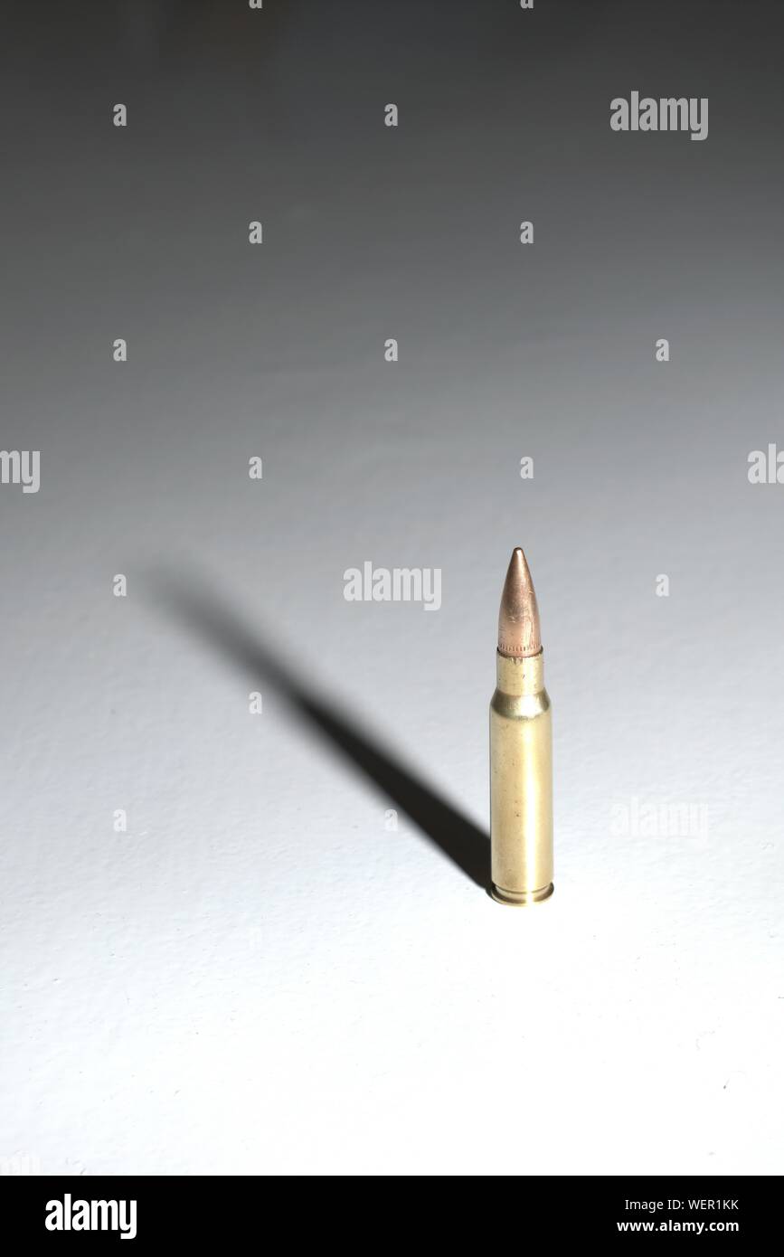 Un grande bullet (7,62 x 51 mm) nato in piedi su una superficie bianca con lunghi drammatico. Lo sfondo è un gradiente di colore nero. Foto Stock