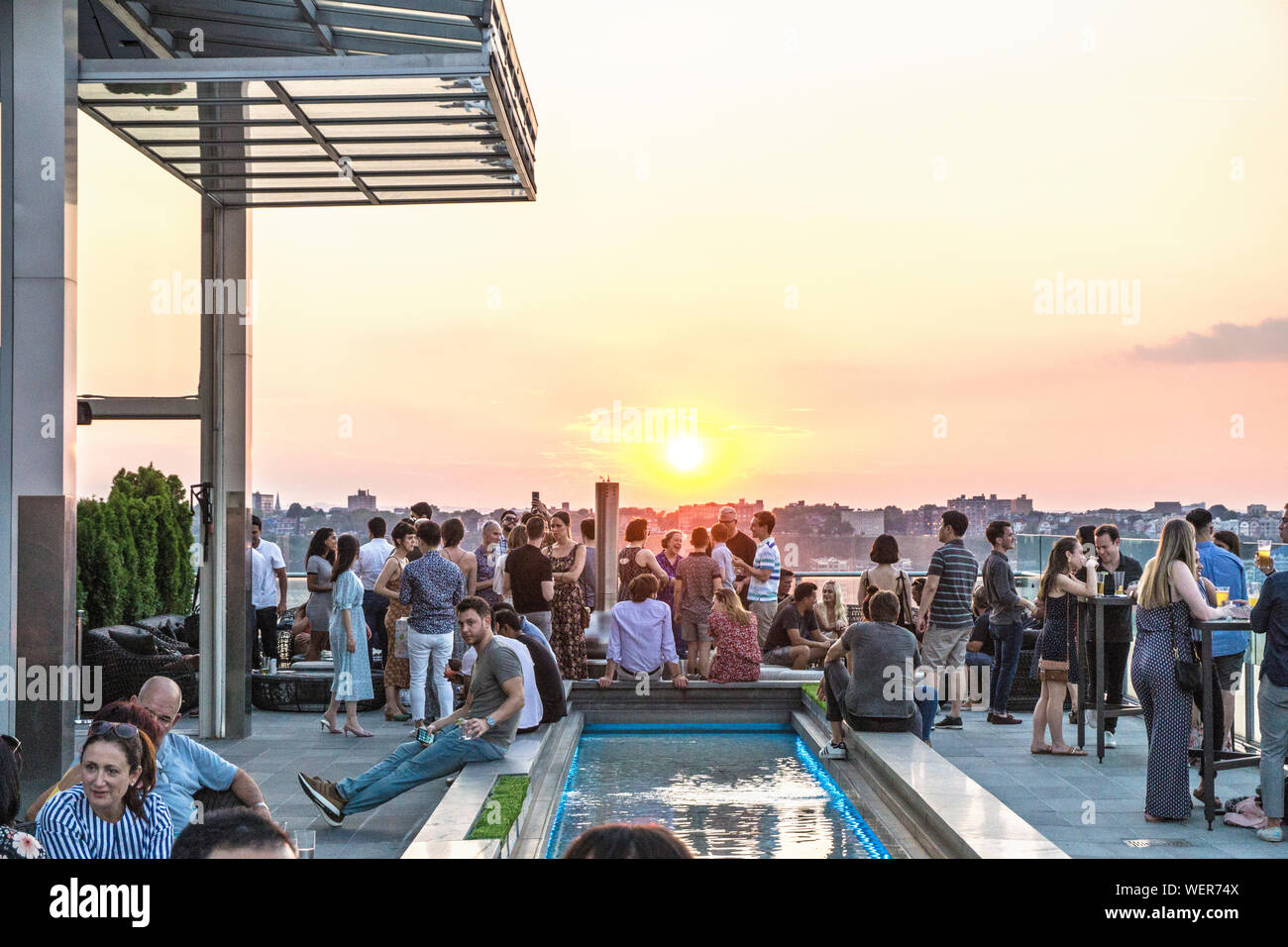 La pace come giovane folla si raduna in sala stampa New York bar sul tetto terrazza per socializzare e sentirsi momento magico quando il sole scivola al di sotto del New Jersey skyline Foto Stock