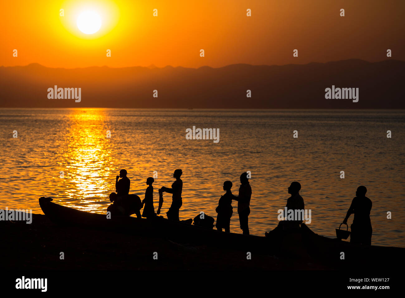 Il lago Malawi a Monkey Bay, gente radunarsi compresi in teh Beach, lavaggio piatti, parlando, rosso tramonto, sud-est-africa Foto Stock