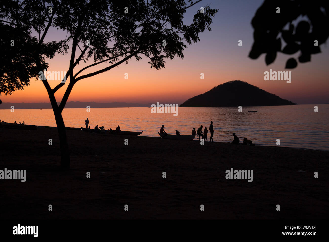 Il lago Malawi a Monkey Bay, gente radunarsi compresi in teh Beach, lavaggio piatti, parlando, rosso tramonto, sud-est-africa Foto Stock