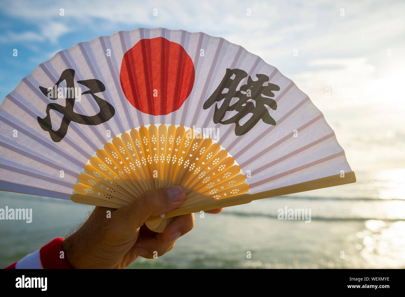 Mano del giapponese sostenitore dello sport tenendo una ventola decorate  con i caratteri kanji compitazione hissho (traduzione inglese: vittoria  certa) di sunrise Foto stock - Alamy