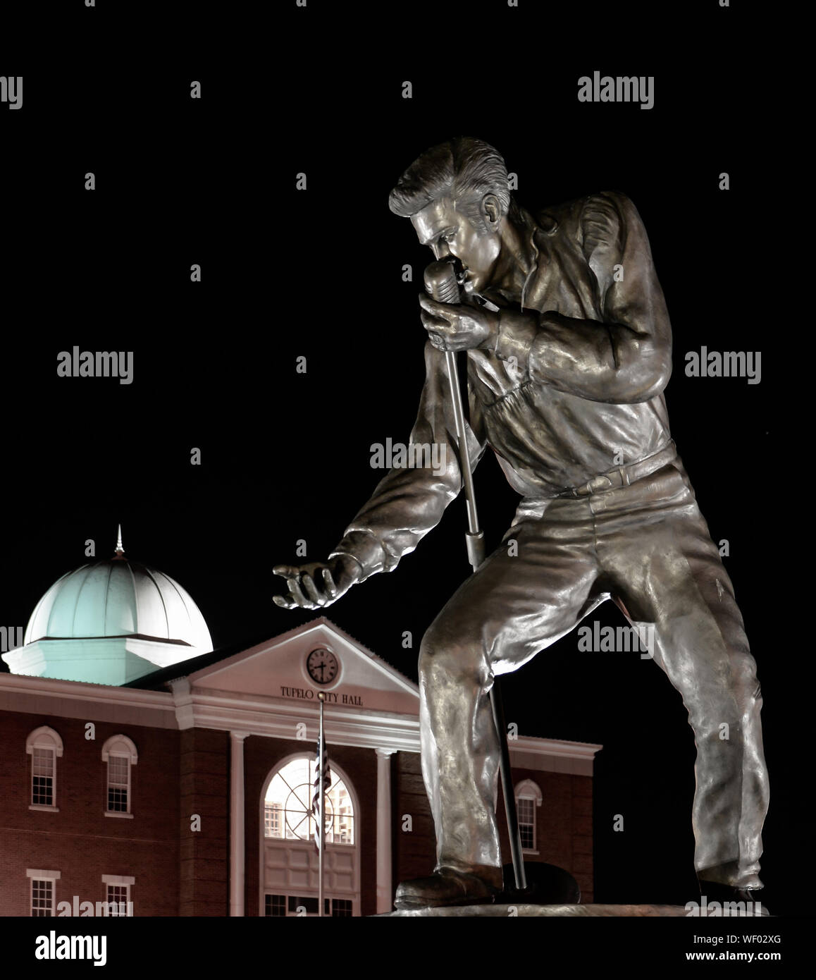 Elvis Presley statua in bronzo posano con microfono e la mano tesa, di notte dalla Tupelo City Hall di Tupelo, MS, STATI UNITI D'AMERICA Foto Stock