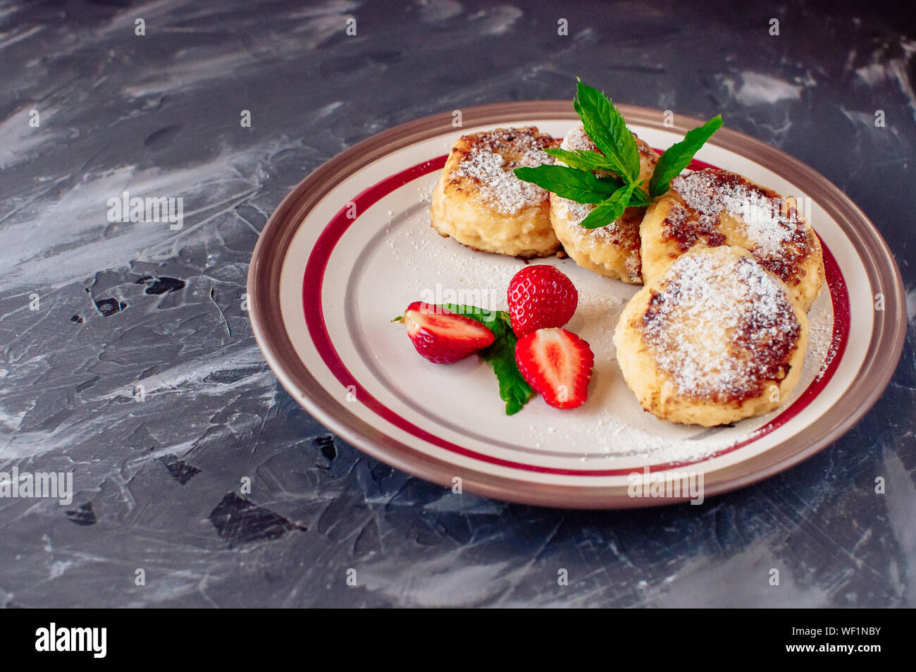 Colazione Gourmet - frittelle di cagliata, cheesecake, cagliata pancake con fragole, menta e zucchero a velo in una piastra bianca. Messa a fuoco selettiva Foto Stock