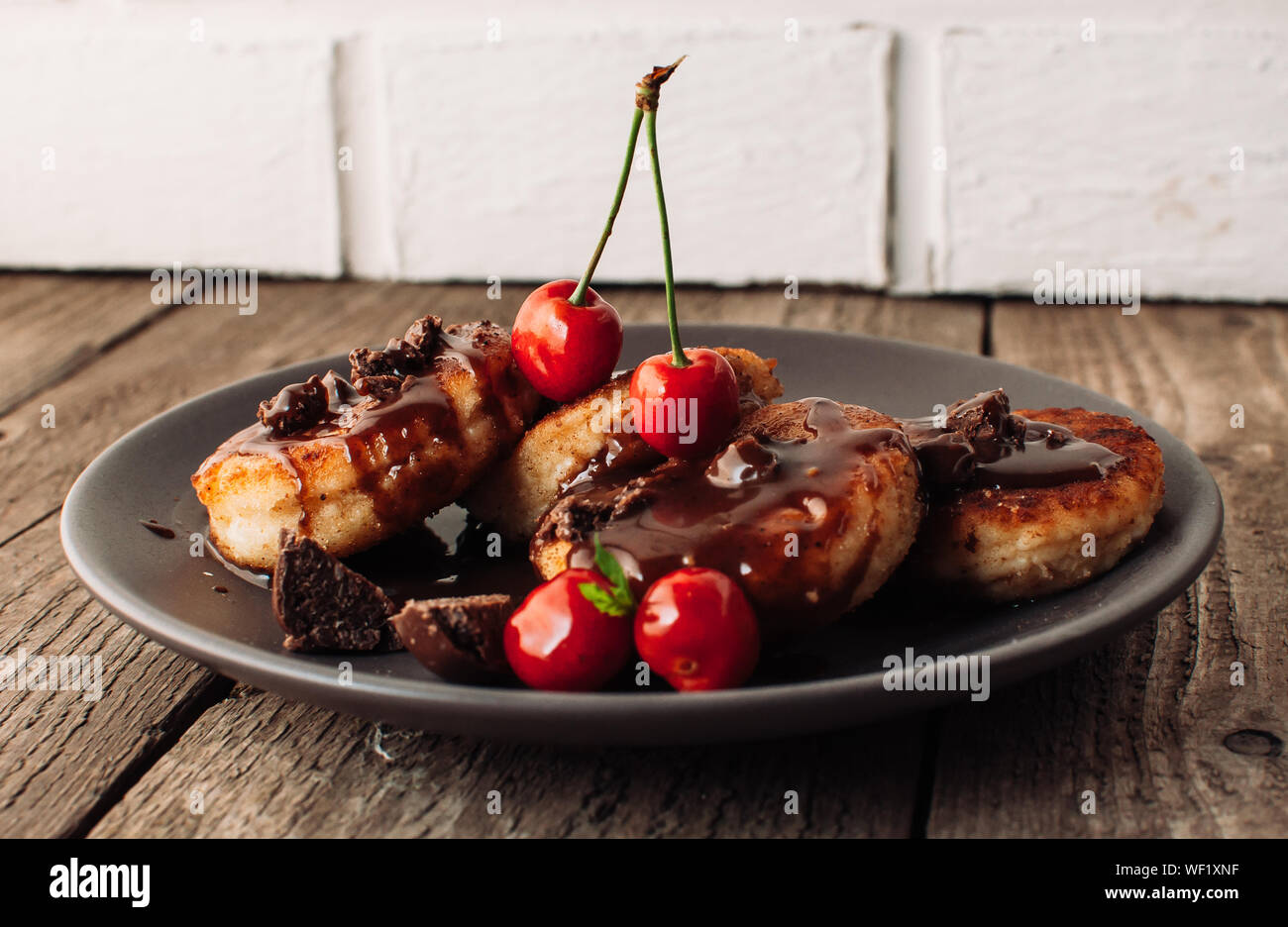 Il cibo della colazione gustosa concetto. La cheesecake, cheesecake, cagliata frittelle con ciliegie e cioccolato su uno sfondo nero da una tabella di cemento e un wh Foto Stock